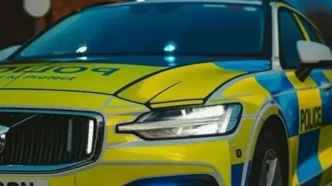 A close up of the front and side of a police car with yellow and blue checked markings  