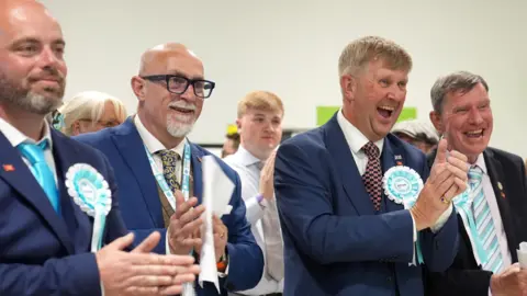 Newly elected Reform UK councillors (left to right) Bradley Thompson, Mark Webster, Peter Harris and Jeff Bray celebrate during the 2026 Essex County Council election at Clacton Leisure Centre in Essex. 