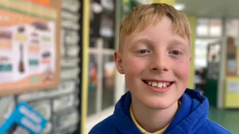 Theo has blond hair, blue eyes and a is wearing a blue school uniform.