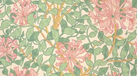The William Morris Society A flower print pattern - called Honeysuckle - comprising of pink flowers with yellow stems and green leaves. 