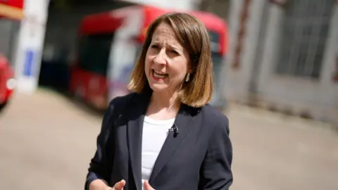 PA Media Technology Secretary Liz Kendall pictured during an interview where she is speaking. She is standing outside. She has short brown hair in a bob-style and she wears a black suit jacket with a white T-shirt underneath.