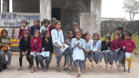 Anshul Verma (Sushila Meena) sits with her students from her school and eats biscuits