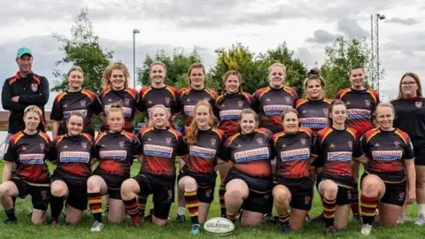 Bridgwater and Albion Rugby Club The Bridgwater and Albion Ladies team in their rugby kits.  They are standing on the pitch looking at the camera. The kits are black, yellow and red.