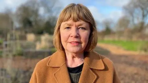 Caroline Williams, pictured wearing a camel-coloured jacket in park