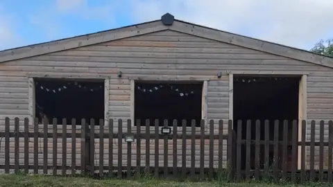 Local Democracy Reporting Service Outside of large wooden outdoor seating shed behind a brown wooden fence. The shed has two large open windows and a open doorway. There are two flood lights attached to the fence.