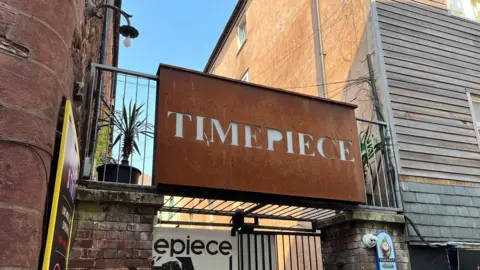 An oxidised metal and white sign for Timepiece above the entrnace to the club