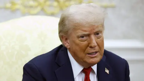 Donald Trump in the Oval Office wearing a blue suit and red tie