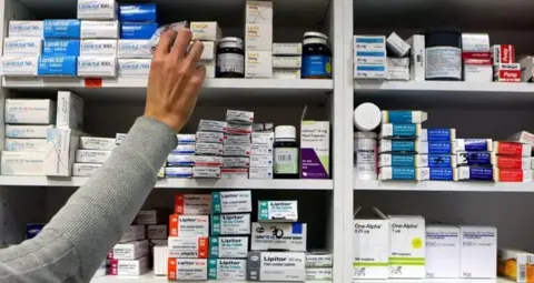 PA A number of medicines on a shelf and a hand at the side reaching for an item