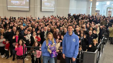 Albert Chait and hundreds of other members of the United Hebrew Congregation wave at a camera.