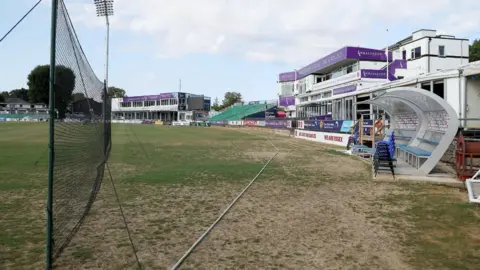 Rhianna Venables/BBC Cricket grounds that has some dry patches. There is a net in the background and spectators grounds 