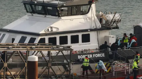 Getty Images Migrants picked up at sea while attempting to cross the English Channel, are escorted off from a UK Border Force boat upon arrival at the Marina in Dover, southeast England, on December 14, 2022