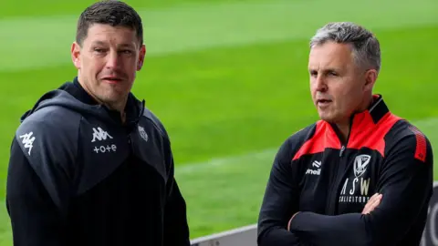 Wigan Warriors coach Matt Peet (left, in black training gear) and St Helens coach Paul Rowley (right, in black and red training top, with arms folded) talk at the side of the pitch before the Challenge Cup semi-final in May.