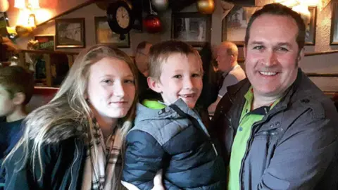 Handout Paul Brand pictured with two children. Mr Brand has short dark hair and is smiling in the photo.