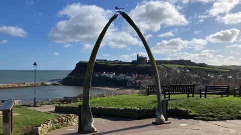 Whitby's Whalebone Arch, two real whale jawbones standing tall and meeting at their tips. Whitby Abbey can be seen in the background between the arch.