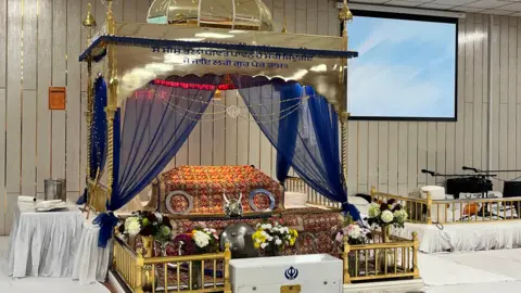 Emma Baugh/BBC Inside the gurudwara - a golden shrine draped with an orange-coloured sheet and blue curtains.