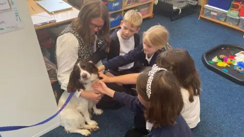 BBC Maya the dog being stroked and cuddled by pupils and a teacher in a classroom 