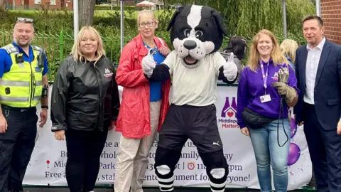 Amelia A group of people stand with a person wearing a dog mascot costume, in front of a Middleport Matters white banner and a blue Canal & River Trust banner