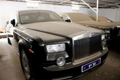 A black Rolls Royce parked at a garage covered in dust