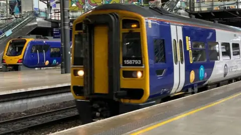 Two Northern trains sit at platforms at Leeds railway station.