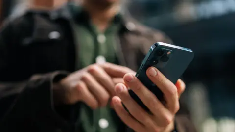 A man wearing dark clothes typing on a smartphone.