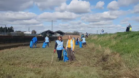 Bruce Langley People holding blue bags and litter-pickers on the grass next to the River Colne in Colchester.