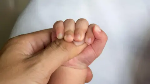 A stock image of a baby's hand being held by an adult human's hand.