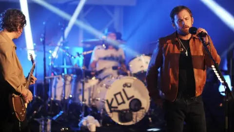 Singer with short brown hair leads a band with a bass drum marked KOL