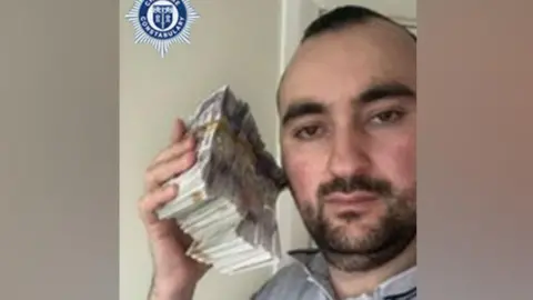 A man is holding a bundle of cash next to his head 