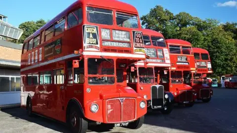 Four bright red heritage buses line up at an angle outside the London Bus Museum in Weybridge