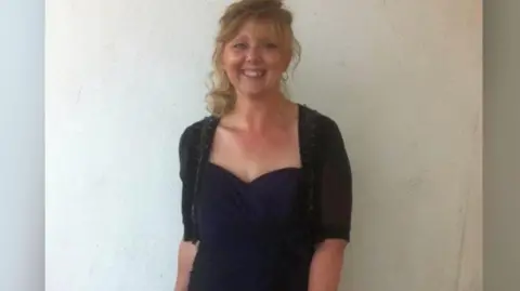 Facebook Kim Older - a woman in her 50s with blonde hair - wears a black cardigan and dress and smiles at the camera.