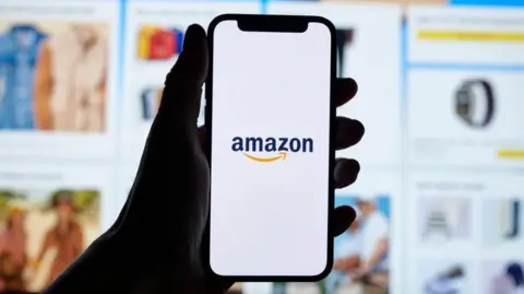 Getty Images A person's hand holds a smartphone displaying Amazon's logo with Amazon website shown in the background.