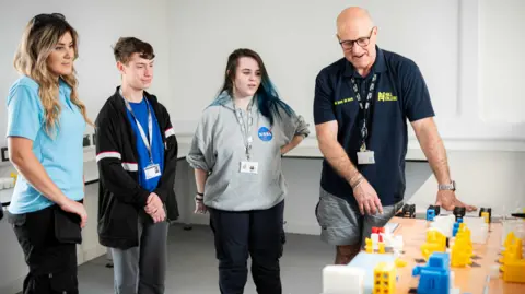 Hull College A male staff member shows three students - two females and one male - a 3D model of the Greenwave facility.