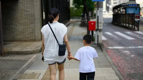 Backview of a mother and her young son holding hands and walking down a street