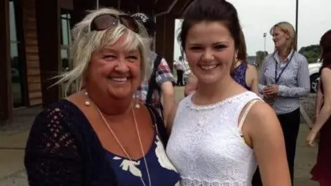 Bethany Sharpe Polly on the left smiling with sunglasses in her hair wearing a blue flowery dress and black cardigan and Bethany next to her smiling in a white lacey dress