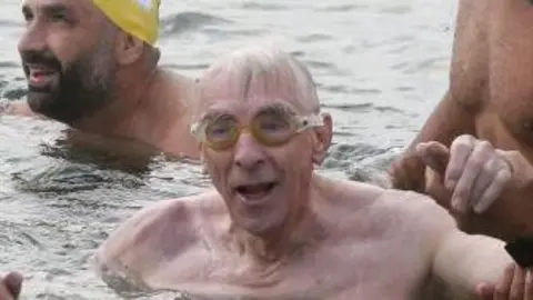 Getty Images Michael Read is pictured at the end of an open water swim. He is being helped by other swimmers. His grey hair is wet against his forehead and he wears goggles.