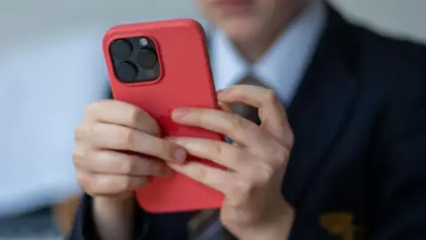 A schoolboy plays on a big, bright red phone. 