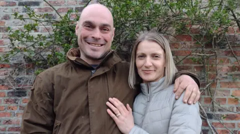 Dorota Spilman Dorota Spilman pictured with her husband. He is bald with blue eyes and is wearing a brown jacket, while Dorota has shoulder-length blonde hair. Both of them are smiling in the photo.