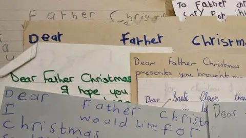 Sheffield University A pile of overlapping letters written by children to Father Christmas.  They are written in blue, green and black ink or pencil. The words Dear Father Christmas can ben seen on five of the letters and there is one letter addressed to Santa Claus 