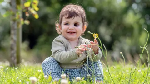 PA Media Nuala Mulholland holding a flower sitting in a field and smiling to the left of the camera