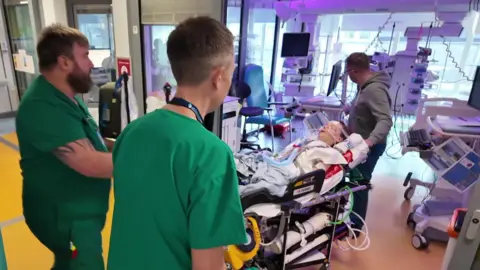 Rex in a hospital bed being wheeled into intensive care