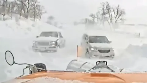 Video taken from inside snowplough shows cars stranded in snow.