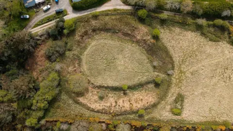 Cornwall Heritage Trust A drone shot of Castilly Henge. It is a large circle with raised ground in the middle, surrounding by trees and fields.