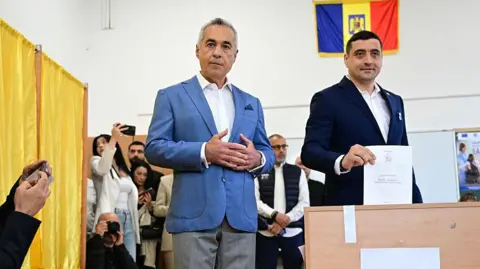 DANIEL MIHAILESCU/AFP Calin Georgescu looks on (L) as George Simion votes