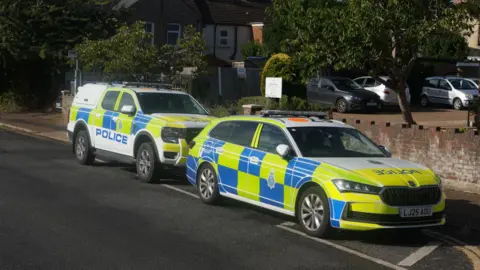 Eddie Mitchell Two police vehicles are parked on the roadside in front of a car park