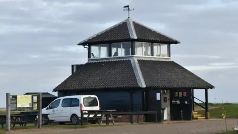 N Chadwick/GEOGRAPH The current visitor welcome point and lookout building at Morston Quay which is a square shaped building with a National Trust sign outside.