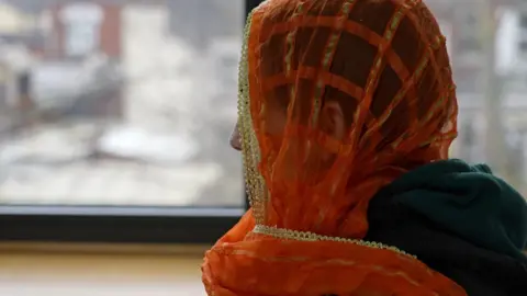 BBC A woman, whose identity cannot be seen, in an orange headscarf looking away from the camera