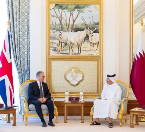 Mofa Qatar via Reuters The two leaders sit opposite each other in a formal room with both UK and Qatari flags either side of the room in front of a regal looking gold framed painting of rams, while in Doha on Friday.