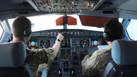 PA Media Two crew members in the cockpit of an RAF Voyager Air-to-Air Refuelling (AAR) aircraft above RAF Akrotiri in Cyprus. The crew members are wearing camouflage boiler suits and headsets.