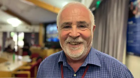 Wearing a blue checked shirt and red lanyard, green councillor Martin Allen stands for a photo at the planning committee in Pershore.