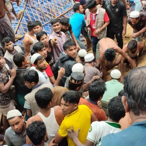 Rohingya Khobor A large crowd gathers around a muddy site as people work by hand to try to rescue people from under the mud